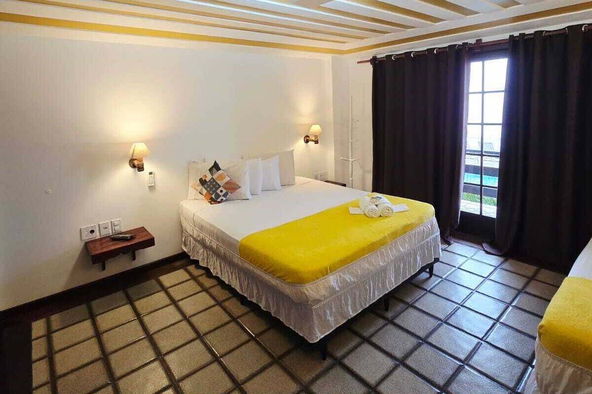A hotel room with a bed, bedside tables, a window with curtains, and a tiled floor.