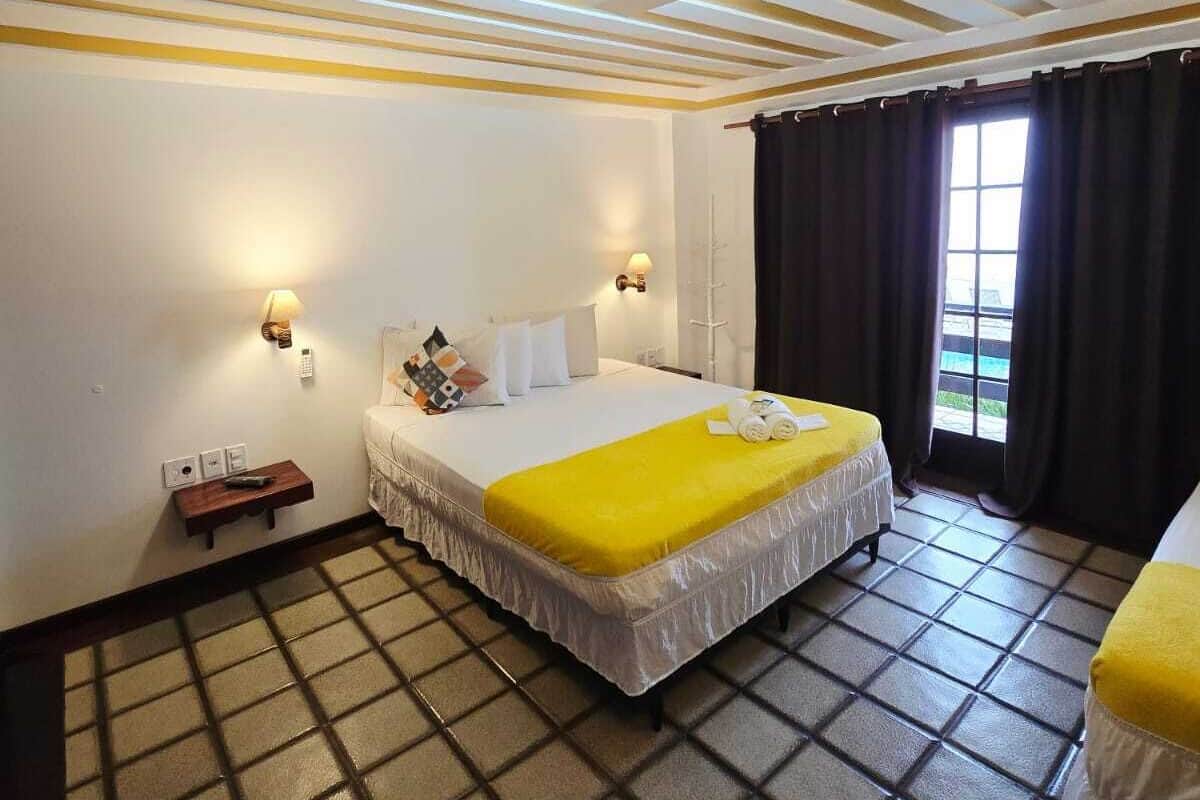 Une chambre d’hôtel avec un lit, des tables de chevet, une fenêtre avec des rideaux et un sol carrelé.