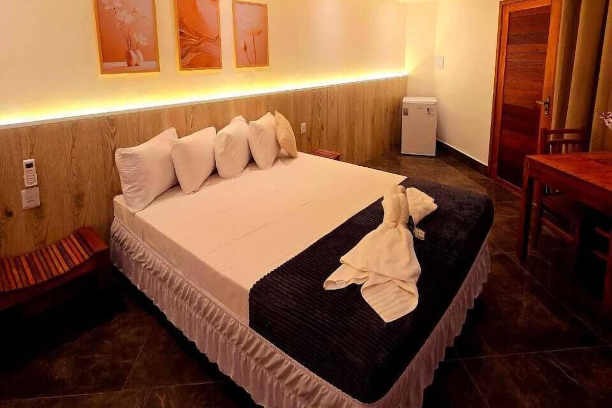 A modern hotel room with a large bed, a wooden headboard, a desk, and a chair.