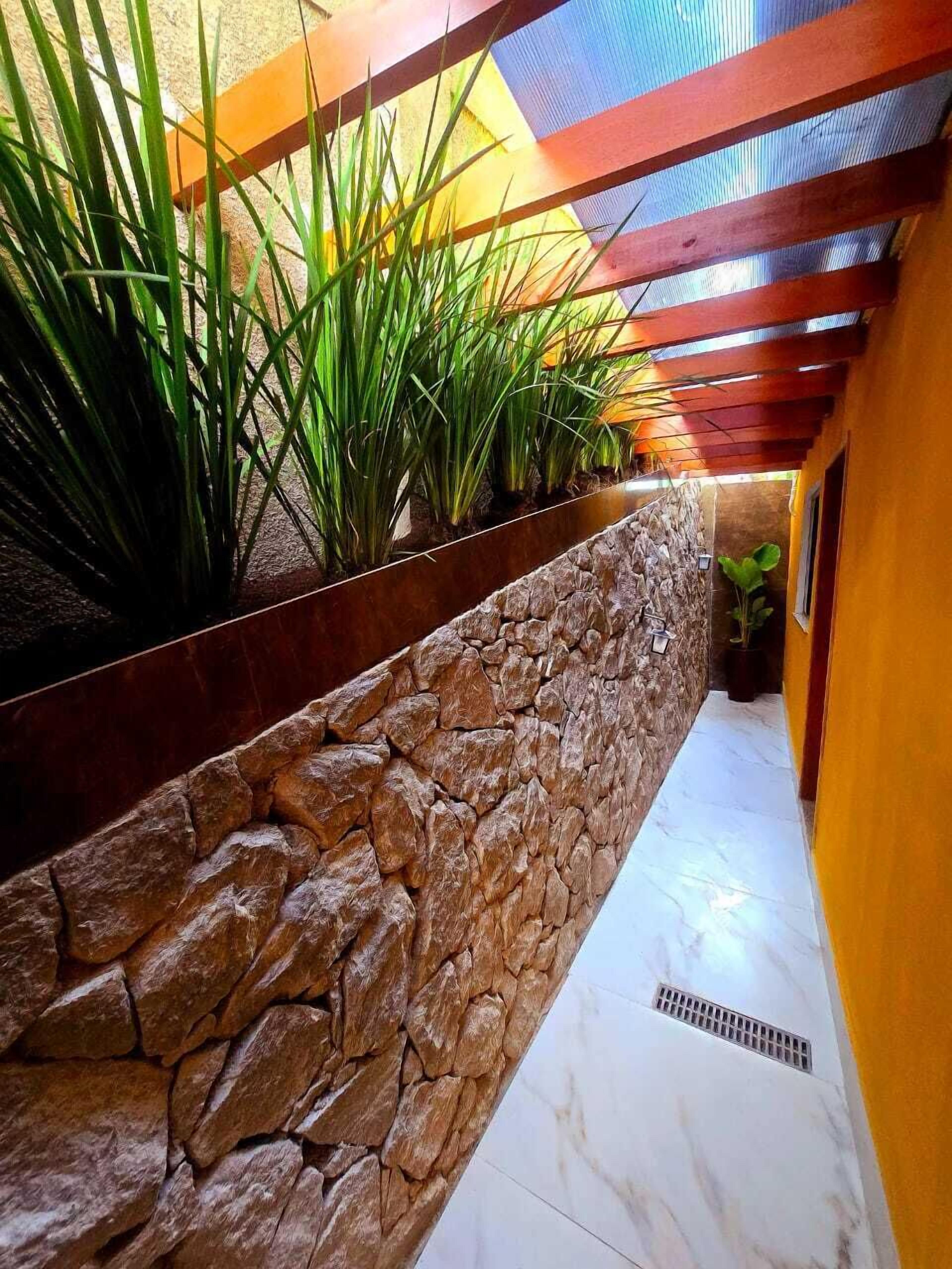 A corridor with a stone wall, a metal planter with green plants, and a tiled floor.