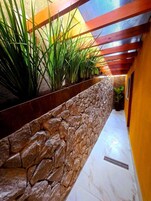 Un pasillo con pared de piedra, una maceta metálica con plantas verdes y suelo de baldosas.