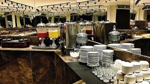Un moderno vestíbulo de hotel con suelo de mármol, un mostrador de recepción y una zona de bufé con platos y vasos.