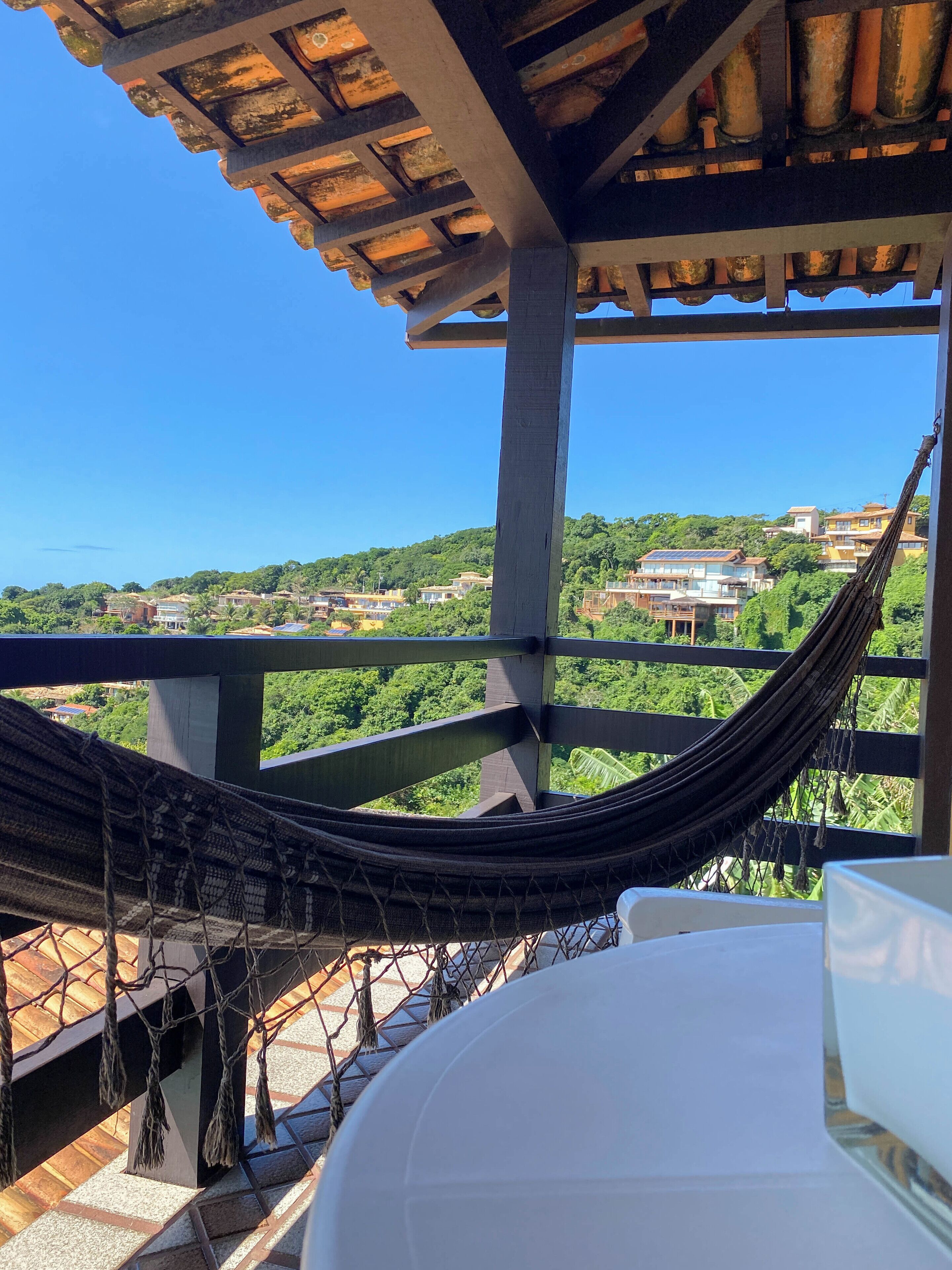 A hammock on a balcony with a view of a residential area and greenery.