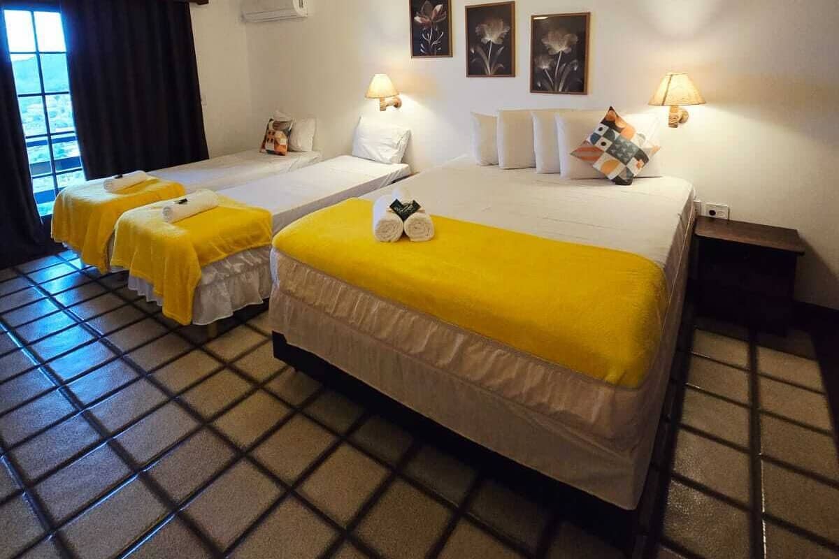 A hotel room with three beds, a tiled floor, and a striped ceiling.