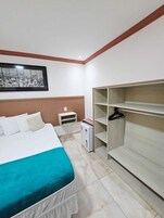Una camera d'albergo con un letto, un armadio, un comodino e un piccolo frigorifero.