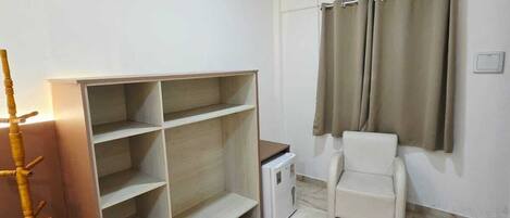 Una habitación con una silla blanca, un perchero de madera, un armario blanco y una ventana con cortinas.