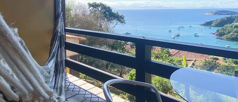Una hamaca en un patio con baldosas, con vistas a la costa, con barcos y follaje.