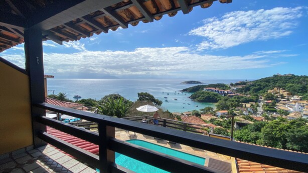 Un balcón con vistas a una piscina, un paisaje costero y barcos a lo lejos.