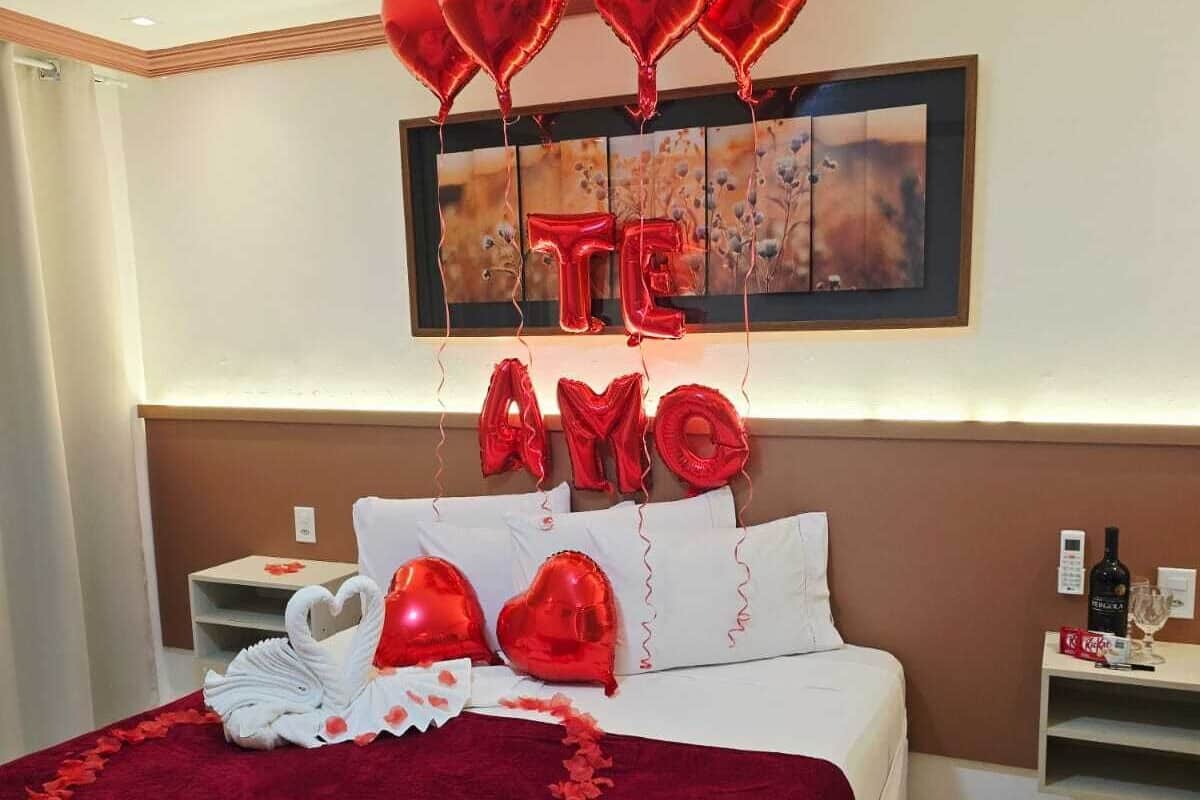 A hotel room with a bed, a nightstand, a framed picture on the wall, and a bottle of wine on the nightstand.