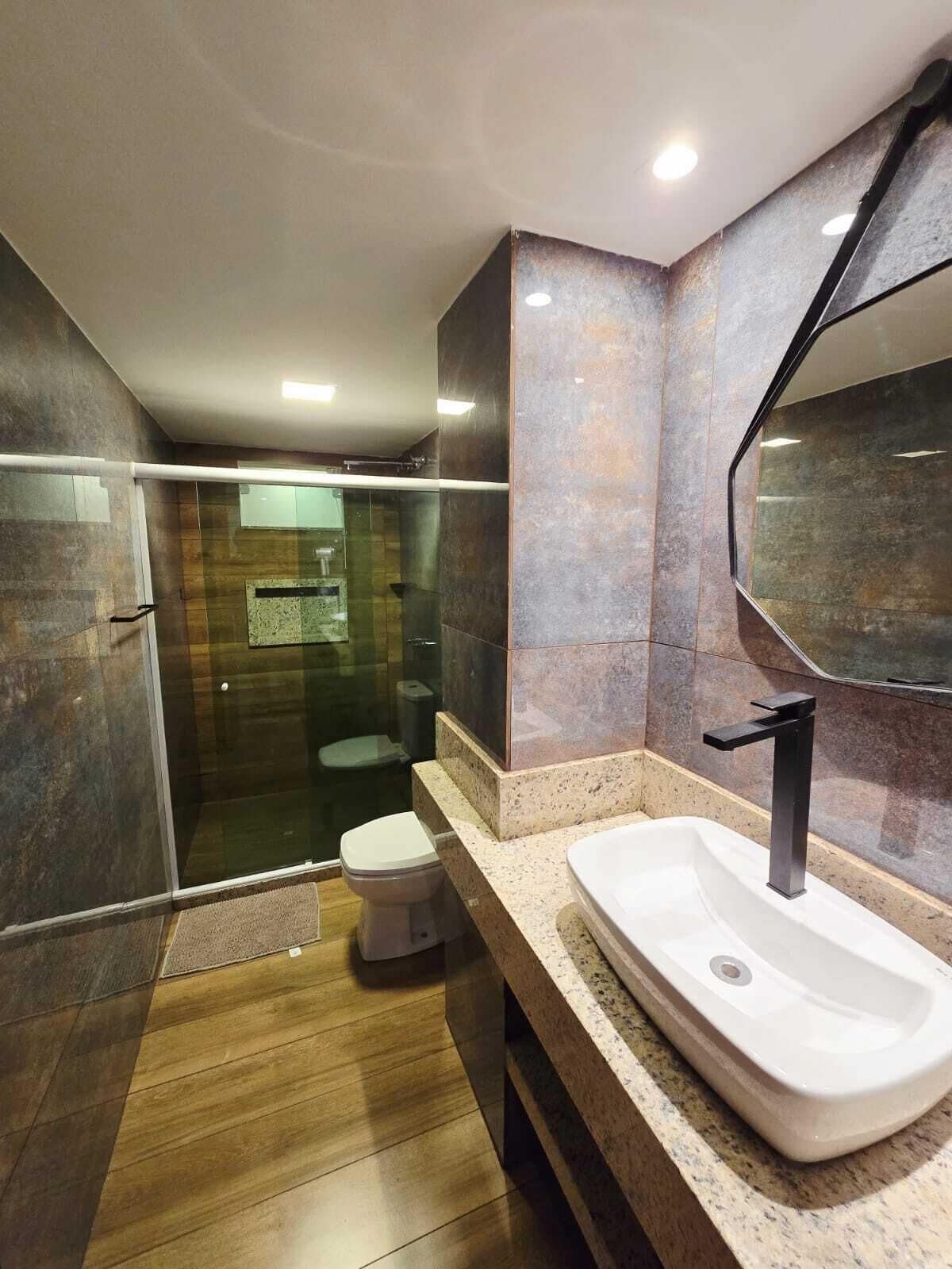 Un bany modern amb dutxa de vidre, un vàter i un lavabo gran amb mirall.