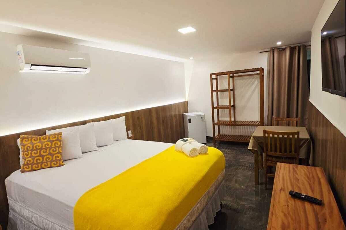 A hotel room with a bed, a desk, a chair, an air conditioning unit, and a window with curtains.