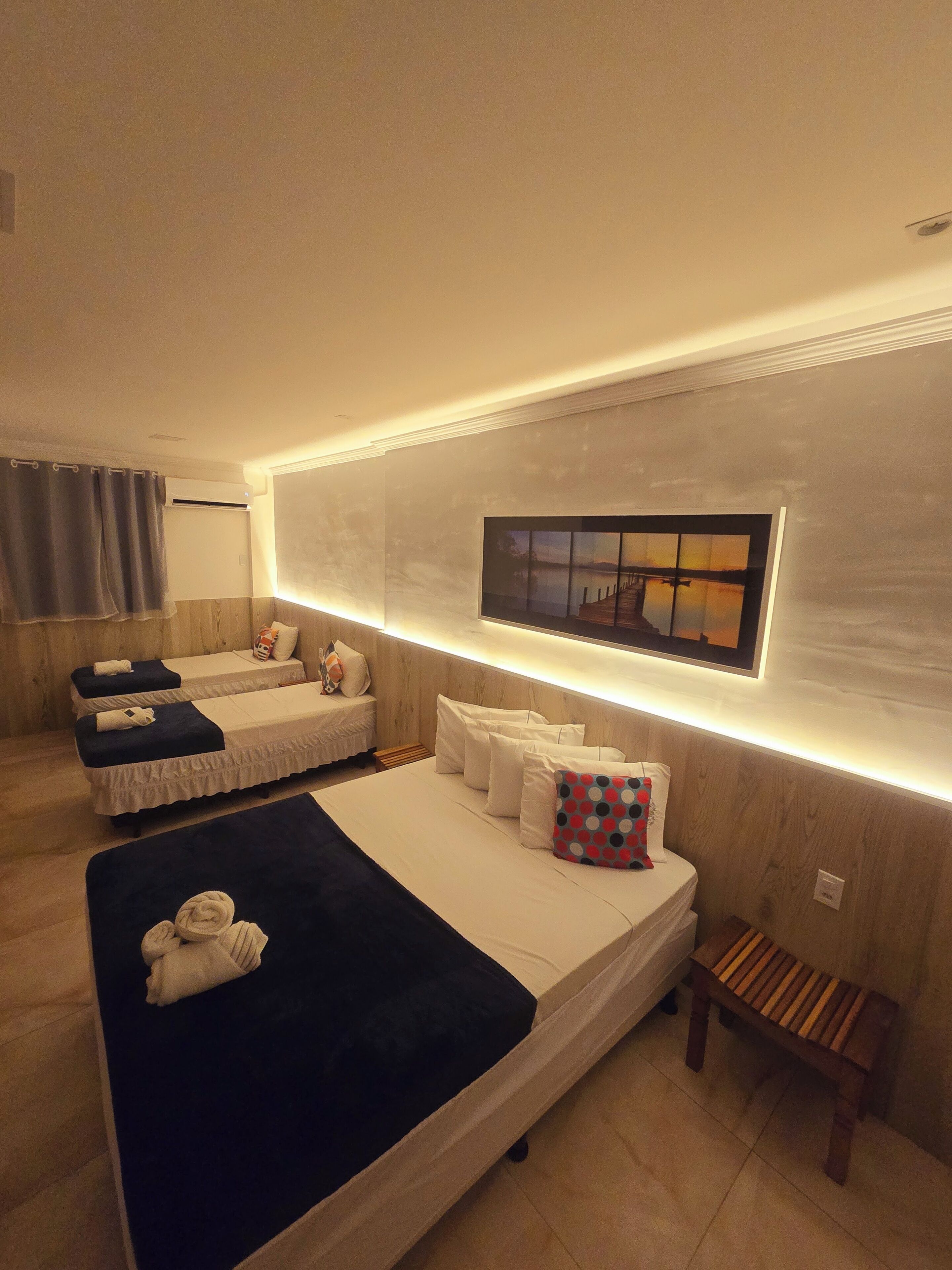 Una moderna camera d'hotel con due letti, una panca, una TV a parete e una lampada a soffitto.