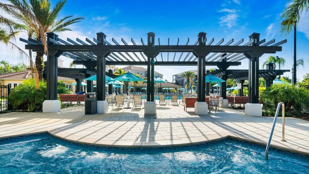 A pool area with a pergola, lounge chairs, and umbrellas. - VCR4-308 - 3BR Condo In Vista Cay near Disney (Orlando)