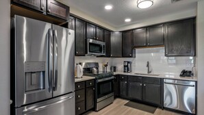 A modern kitchen with stainless steel appliances, dark wood cabinets, and a tiled backsplash. - VCR4-308 - 3BR Condo In Vista Cay near Disney (Orlando)
