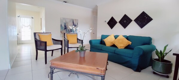 Ein Wohnzimmer mit einem türkisfarbenen Sofa, zwei Sesseln, einem Couchtisch und einer Topfpflanze.