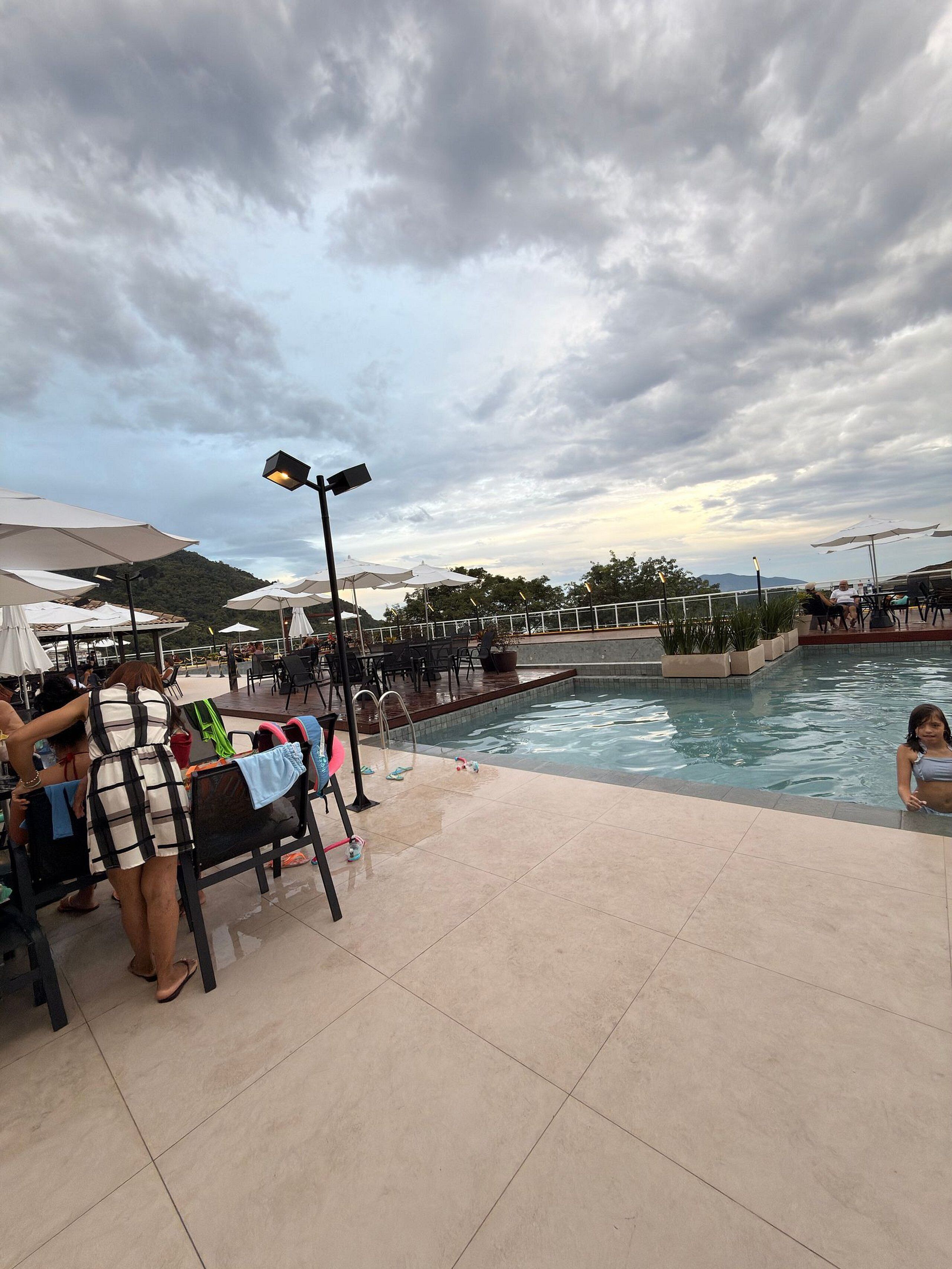 A poolside area with lounge chairs and umbrellas, a pool, and a view of the surrounding landscape.