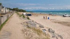 Une plage de sable avec une promenade en bois, des personnes se promenant sur la plage et des véhicules.