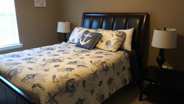 Una cama con una colcha de motivos náuticos, dos lámparas de noche y un adorno en la pared sobre la cama.