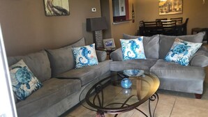 Una sala de estar con un sofá seccional gris, una mesa de centro de vidrio y almohadones decorativos.