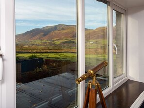 A telescope on a tripod by a window overlooking a rural landscape with hills. - Flaska House (Penrith)