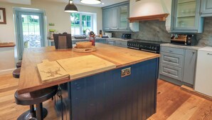 A modern kitchen with a large island, dark blue cabinets, and a built-in oven. - Flaska House (Penrith)