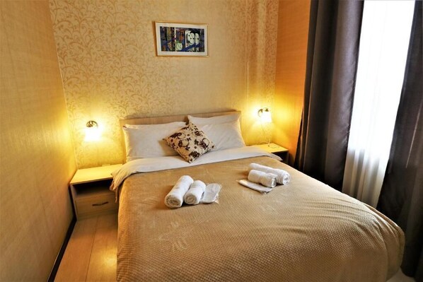 A neatly made bed with a floral pillow, two bedside lamps, and rolled towels on the bed. - Unique and Cozy Apart Hotel on the corner of London Park in Tbilisi (T'bilisi)