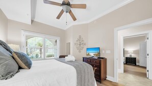 A bedroom with a bed, a ceiling fan, a TV, and a dresser.