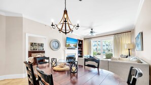 A dining area with a round wooden table, black chairs, a chandelier, and a view of the outdoors through large windows.