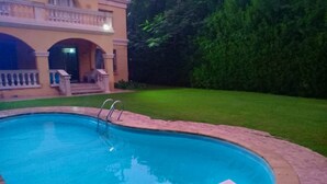 A swimming pool with a stone border, a small deck area, and a well-maintained lawn.