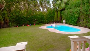 A backyard with a swimming pool, a patio table, and a small gazebo.