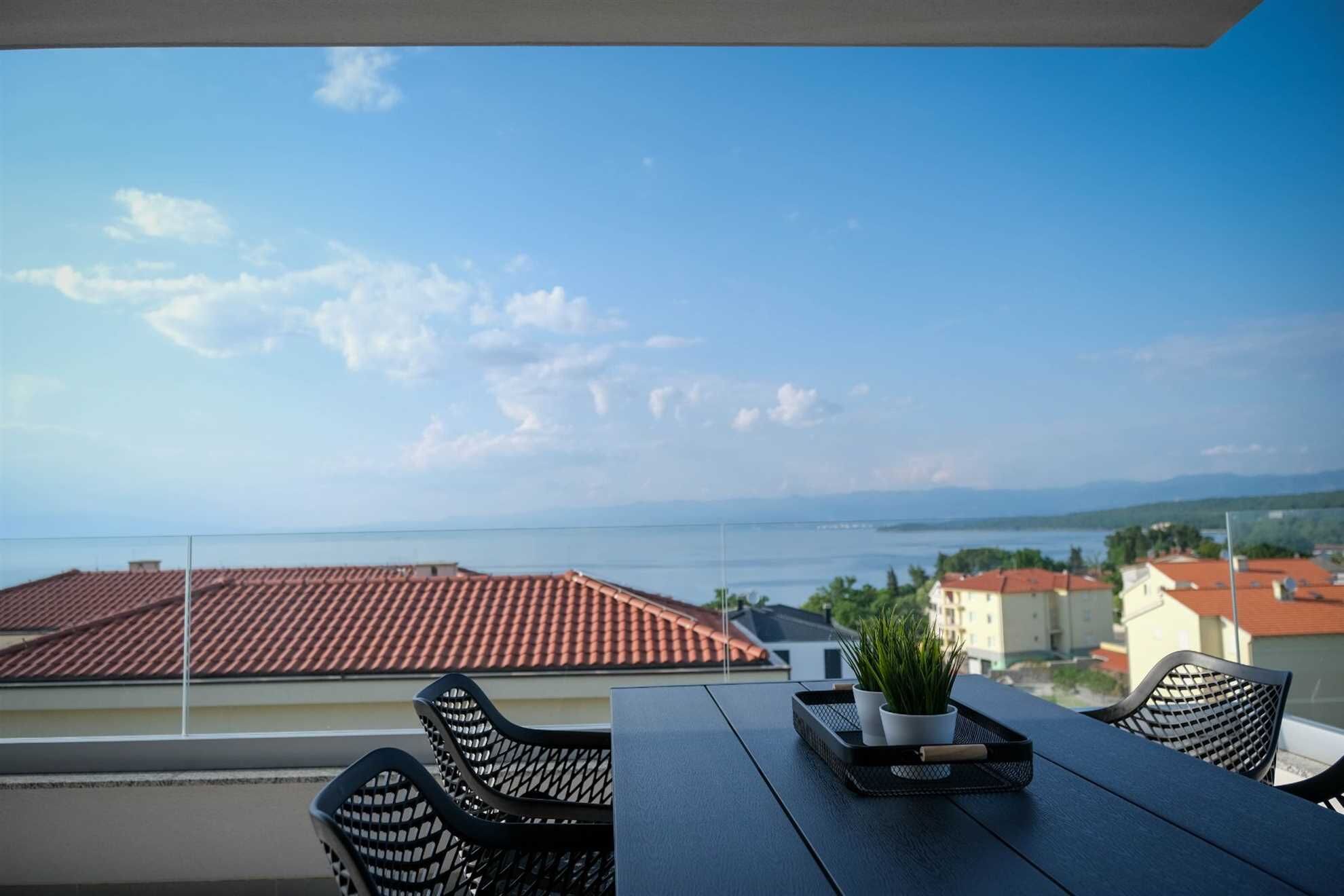 Un balcón con mesa y sillas, con vista al litoral, edificios y una extensión de agua.