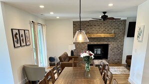 A spacious dining area with a wooden table and chairs, a hanging pendant light, and a brick fireplace in the background.
