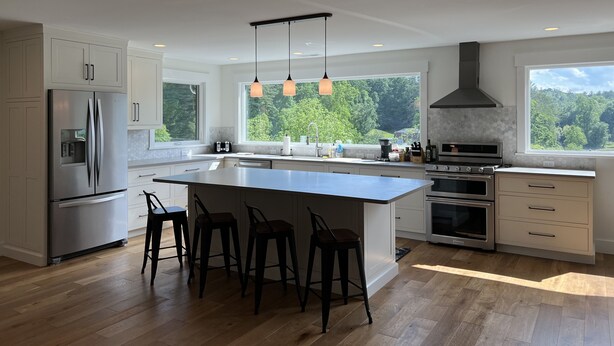 A modern kitchen with a large island, stainless steel appliances, and a view of the forest.