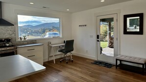 A modern kitchen with a large window, wooden flooring, a dining area, and a bench.