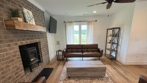 A living room with a brick fireplace, leather sofas, a wooden coffee table, and a ceiling fan.