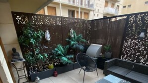 A covered patio area with a seating arrangement, including a sofa and chairs, a small table, and potted plants. - Appart Avec Garage et Terrasse Thier Buffon (Avignon)