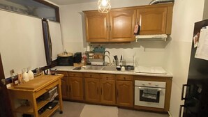 A compact kitchen with wooden cabinets, a built-in oven, and a refrigerator. - Appart Avec Garage et Terrasse Thier Buffon (Avignon)