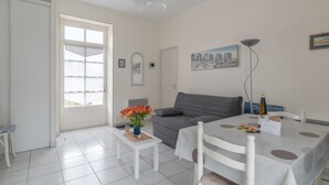 A spacious living room with a grey sofa, a white coffee table, and a dining table with a white tablecloth. There is a door leading to a balcony, and a painting on the wall. - La Birochère - 400 m plage - Parking (Pornic)
