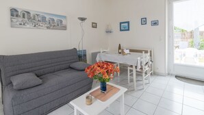 A modern living room with a grey sofa, a white coffee table with a vase of flowers, a dining table with chairs, and a large window with a view of the outdoors. - La Birochère - 400 m plage - Parking (Pornic)