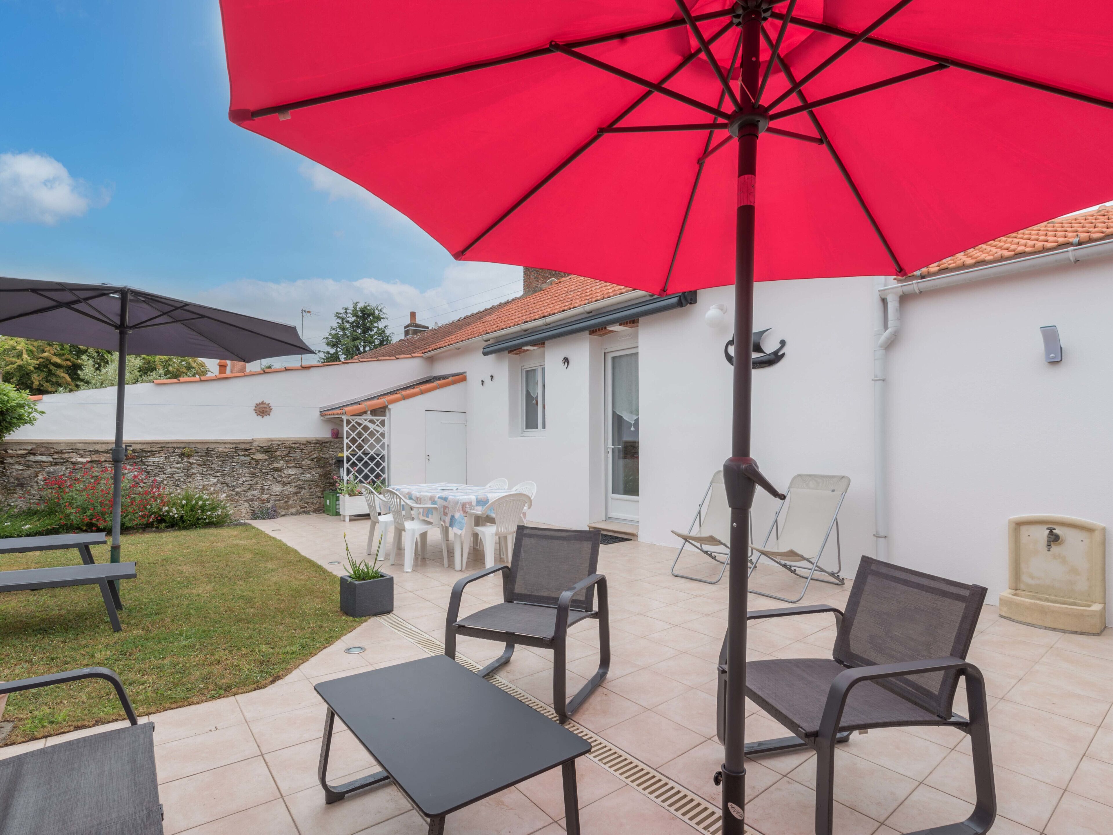 An outdoor patio area with a red umbrella, two black tables, and four chairs.