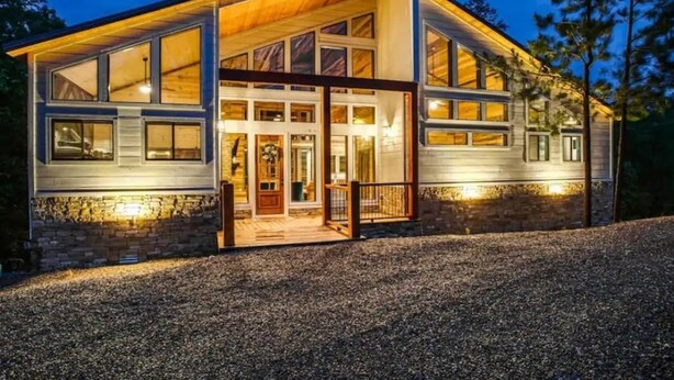 Una casa moderna con amplios ventanales, una terraza de madera y un cimiento de piedra.
