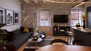 A modern living room with a stone wall, a sofa, a coffee table, a TV, and a dining area with chairs.