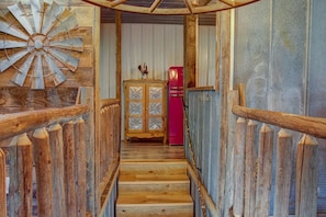 Een houten trap met een landelijke uitstraling, die leidt naar een kamer met een rode koelkast en een decor kast.