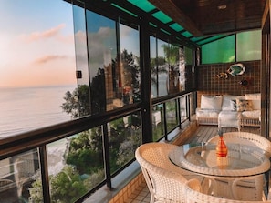 A balcony with a glass railing, wicker furniture, and a view of the sea.