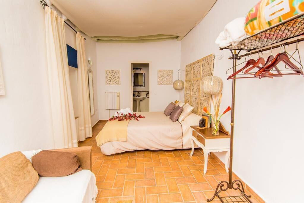 A bedroom with a bed, a bedside table, a hanging clothes rack, and a view into the bathroom.