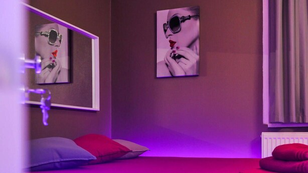 Un dormitorio con cama, almohadas rojas, un espejo y dos obras de arte colgadas en la pared.