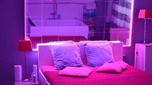 Un dormitorio moderno con un espejo grande, una colcha roja y un cabecero blanco.