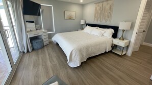 Quarto com cama, mesas de cabeceira, escrivaninha, cadeira, ventoinha no teto e janela com cortinas.