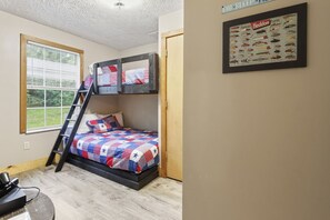 Una cama litera con colcha, una escalera, una ventana con persianas y un cuadro con un diagrama de señuelos de pesca en la pared.