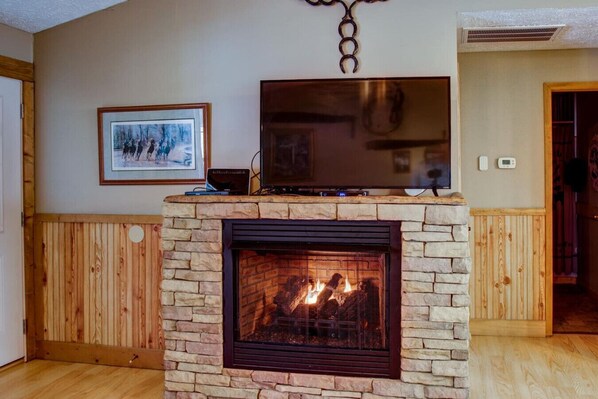 Una sala de estar con chimenea de piedra, un televisor sobre un mueble bajo y un cuadro en la pared.